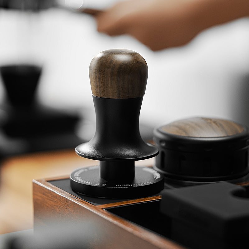 MHW-3BOMBER Flash Tamper 2.0 tamper en nogal/negro (Walnut/Black) con mango de nogal, apoyado en una estación de compactado