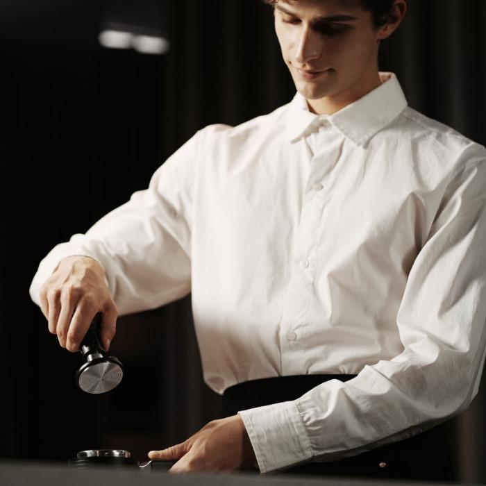 MHW-3BOMBER Yu Series Impact Tamper tamper en noir avec base en inox dans la main d’un barista