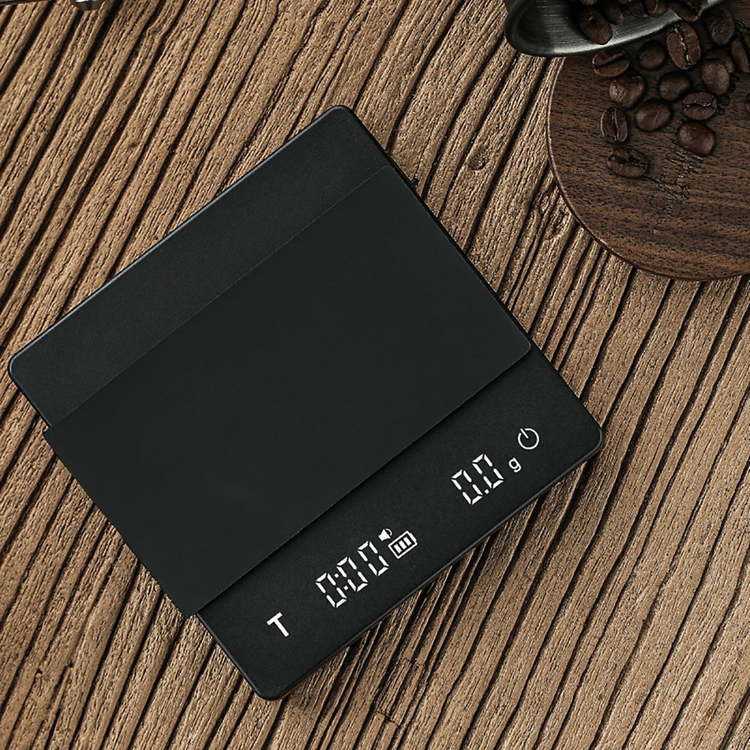 Balance à café MHW-3BOMBER Cube 2.0 en noir (Black) avec tapis en silicone posé et affichage du temps et du poids