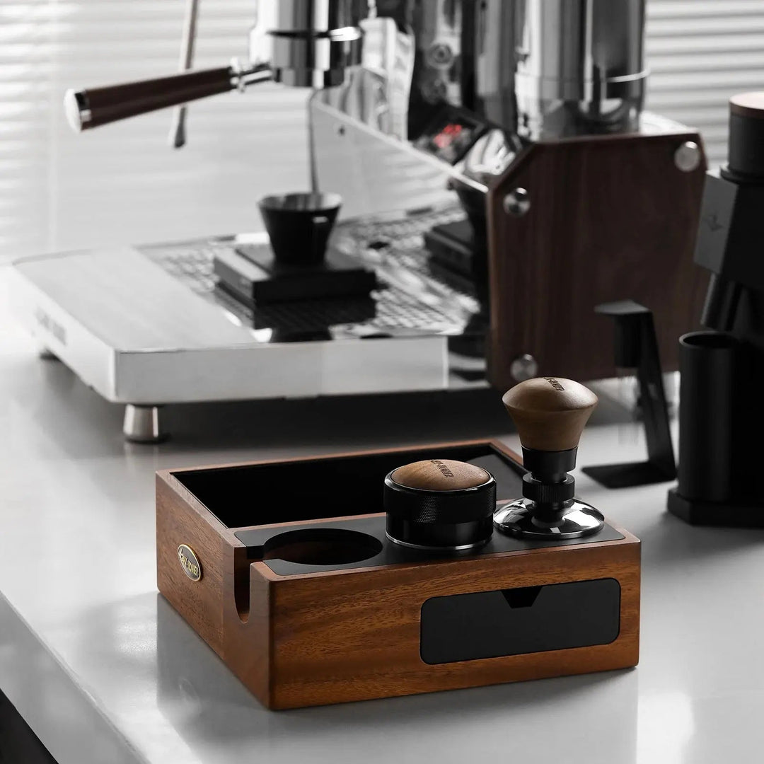MHW-3BOMBER knock box multifonction en noyer et noir (Walnut/Black) avec tasseur et distributeur devant la machine espresso