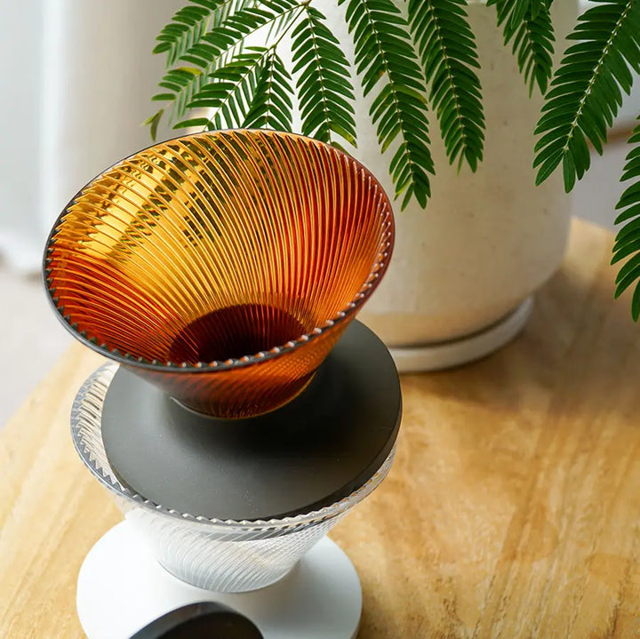 Hario V60 Dripper NEO 02 Pour-Over Brewer in Bernstein (Amber) auf einer Kaffeekaraffe auf einem Holztisch neben einer Zimmerpflanze