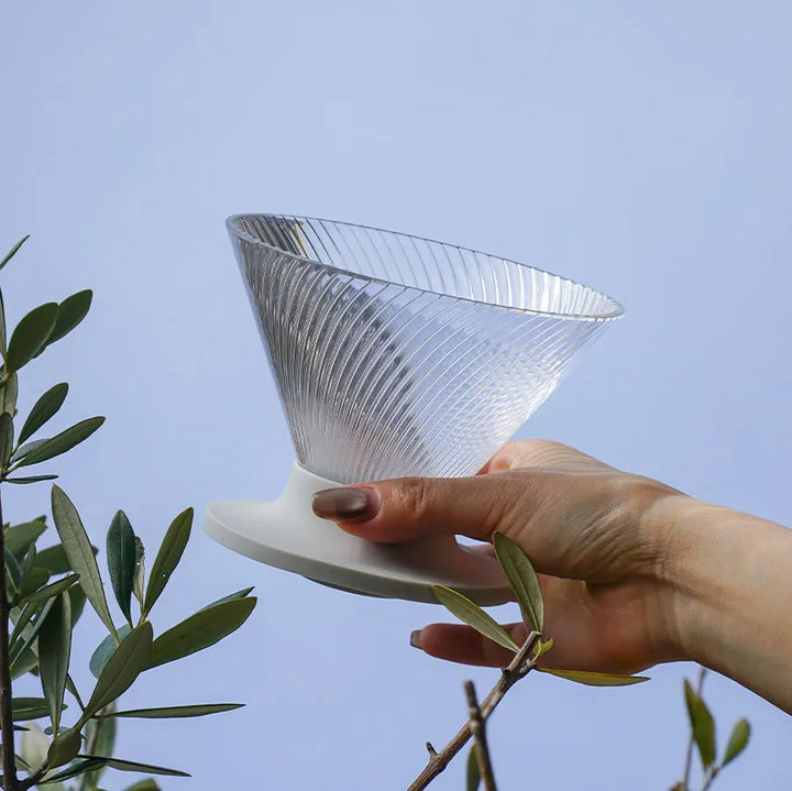 Hario V60 Dripper NEO 02 Pour-Over Brewer in Transparent in der Hand gegen den Himmel gehalten, durchscheinendes Tritan