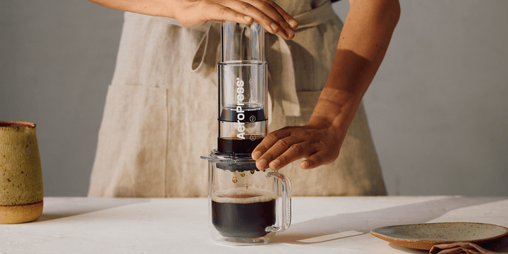 AeroPress Clear Kolben wird von Hand auf einem Glasbecher heruntergedrückt – Coffee Coaching Club 21