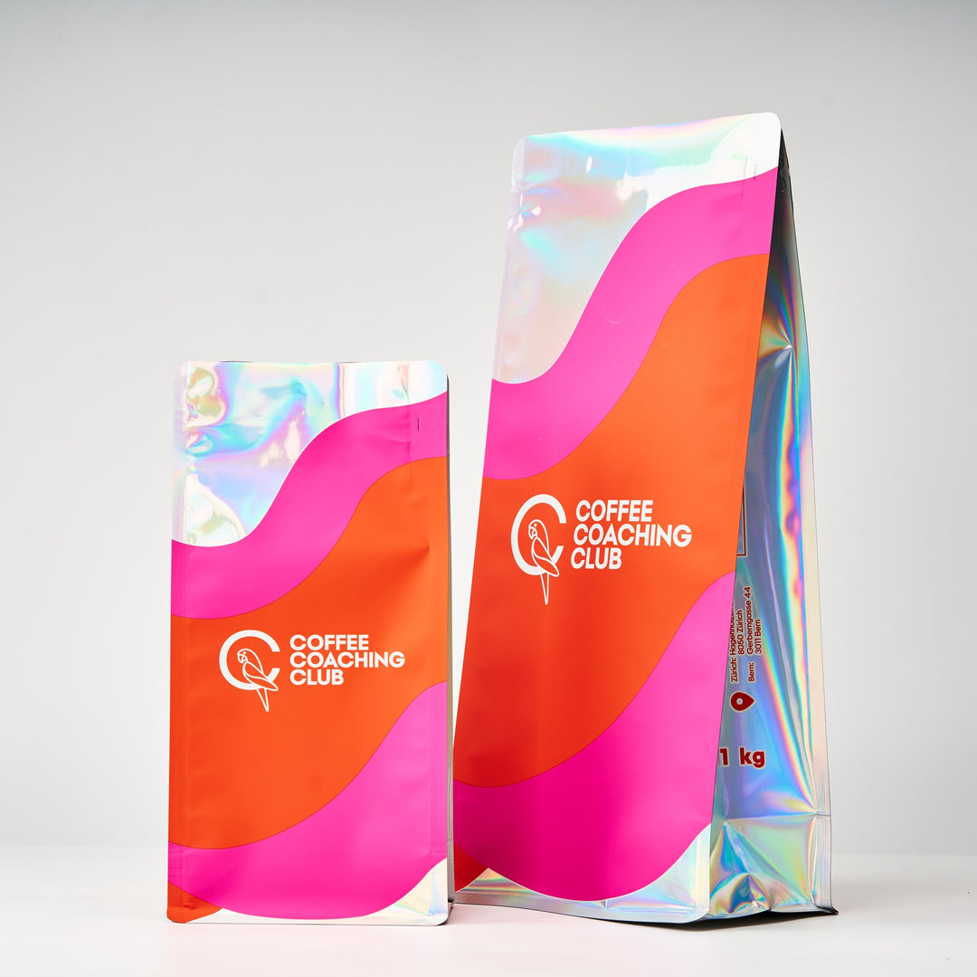 Caffè in grani Bright Cassis – sacchetti da 250 g e 1 kg a confronto, vista laterale, design rosa e arancione – Coffee Coaching Club