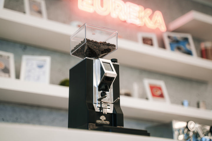 Eureka Mignon Specialità Schwarz auf der Theke vor Regal mit Eureka-Leuchtschrift – Coffee Coaching Club 19
