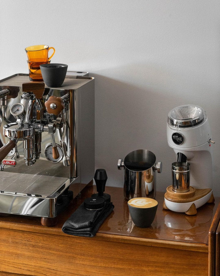 Normcore Tamper de presión regulable junto a una máquina de espresso, un molinillo y un cappuccino – Coffee Coaching Club 10