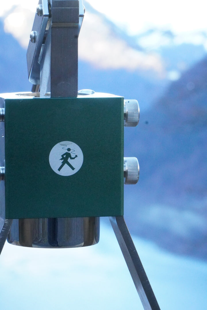 Olympia Express Mina Grün Brühkammer mit Logo vor Bergsee – Coffee Coaching Club 58